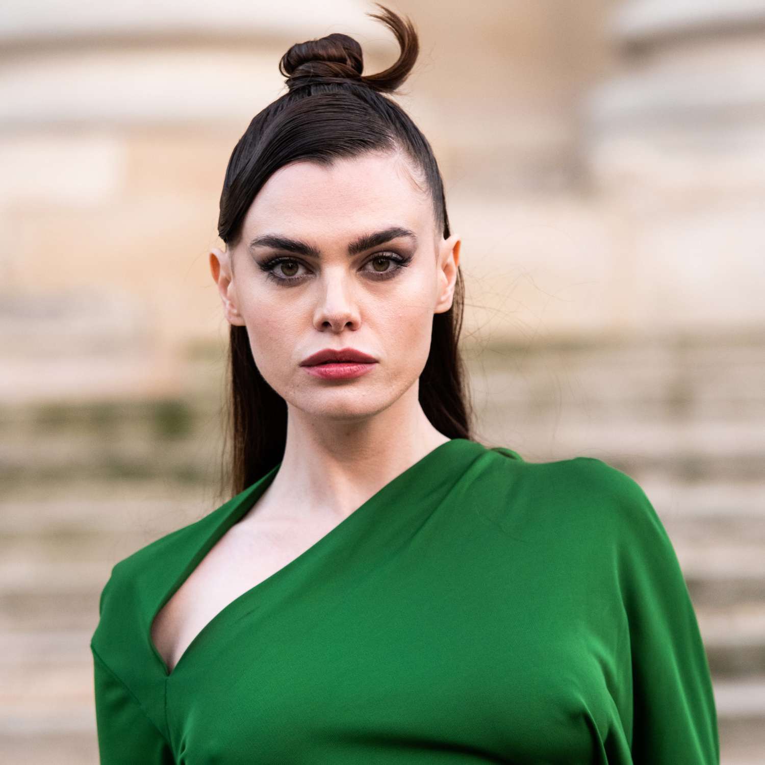 zoomed in picture of Charli Howard looking at camera with bangs in deep side part slicked behind ear, straight hair and top section pulled back tightly into structural bun with ends left out and curled