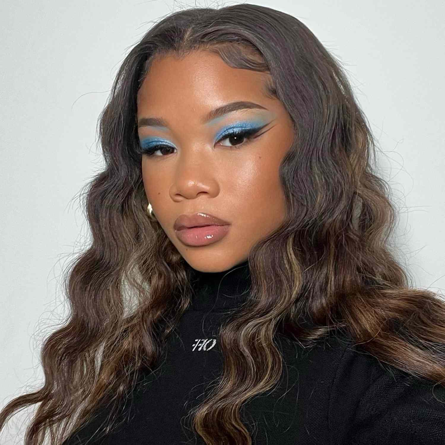 Storm Reid wears a defined wavy hairstyle and blue eyeshadow