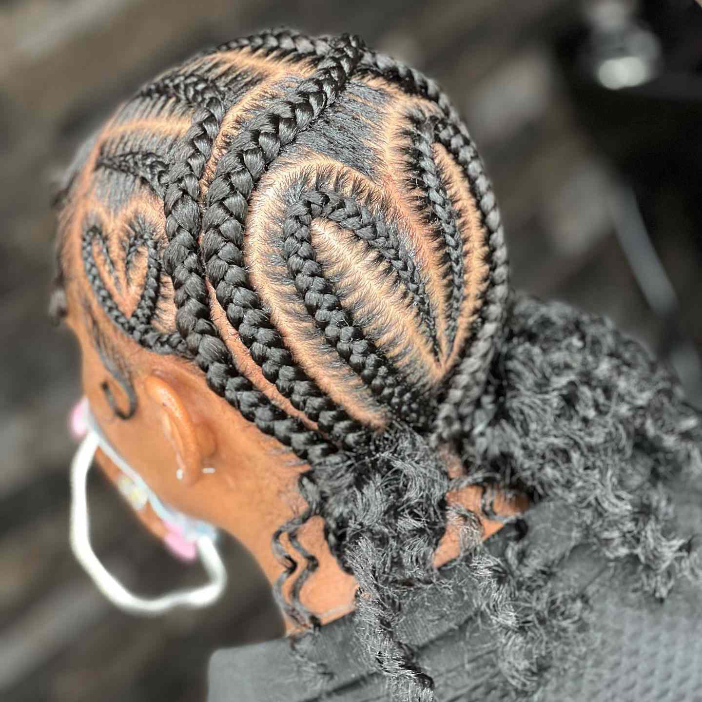 The back of a woman's head, a braided heart visible, the bottom of her hair loose and curly