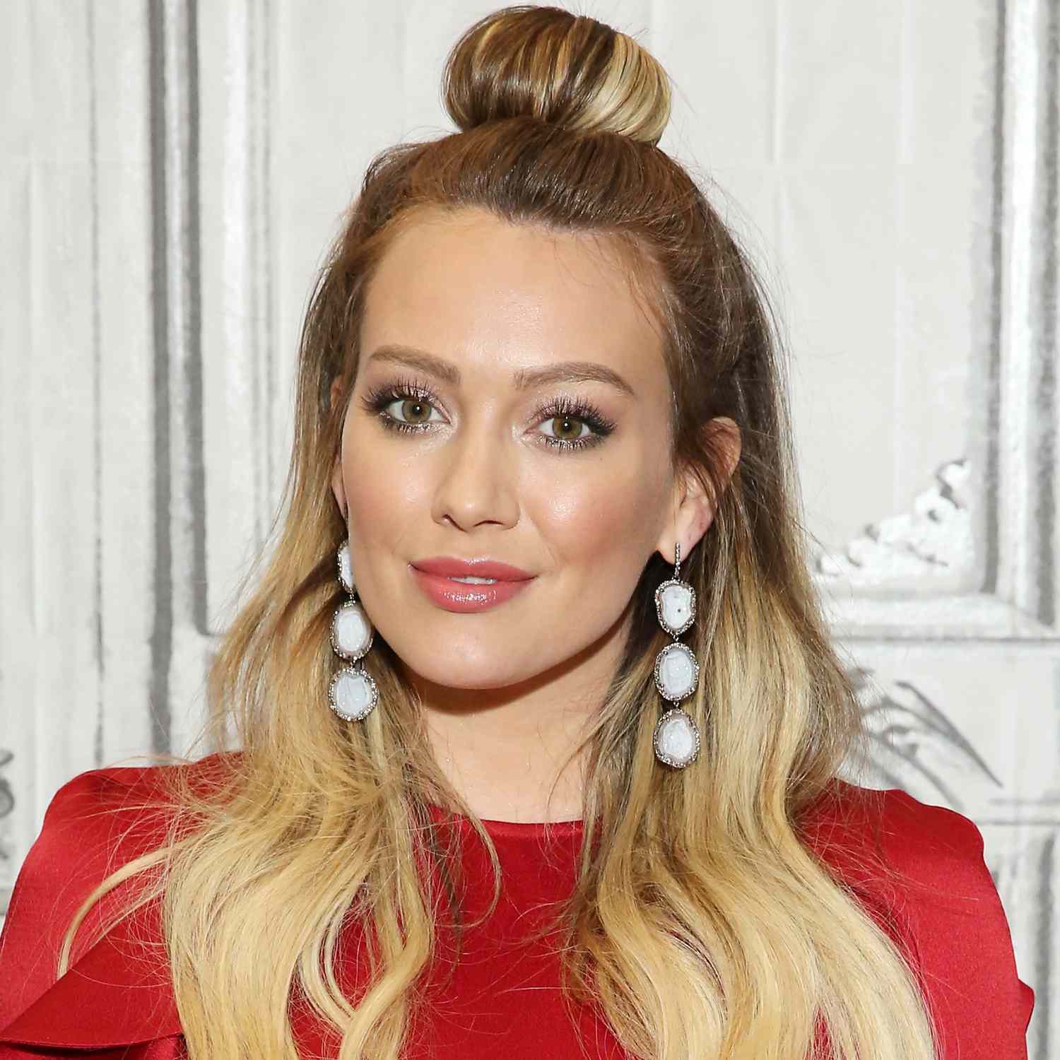 Hilary Duff looking at camera, zoomed in picture of blonde rooty hair in soft waves, with top crown section piled into donut bun on top of head