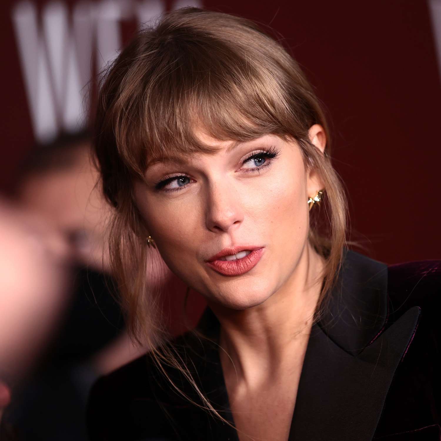 Taylor Swift wears a low updo hairstyle with bangs and wispy face-framing layers