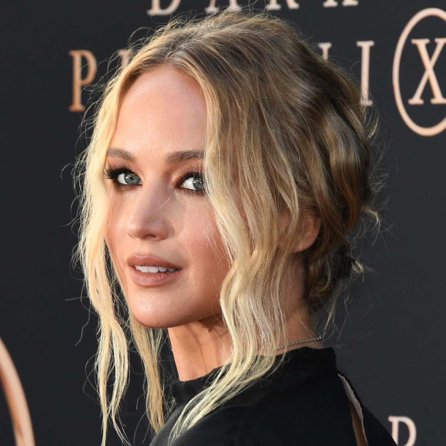 Jennifer Lawrence wears a low bun hairstyle with wavy face-framing pieces and shimmery eyeshadow