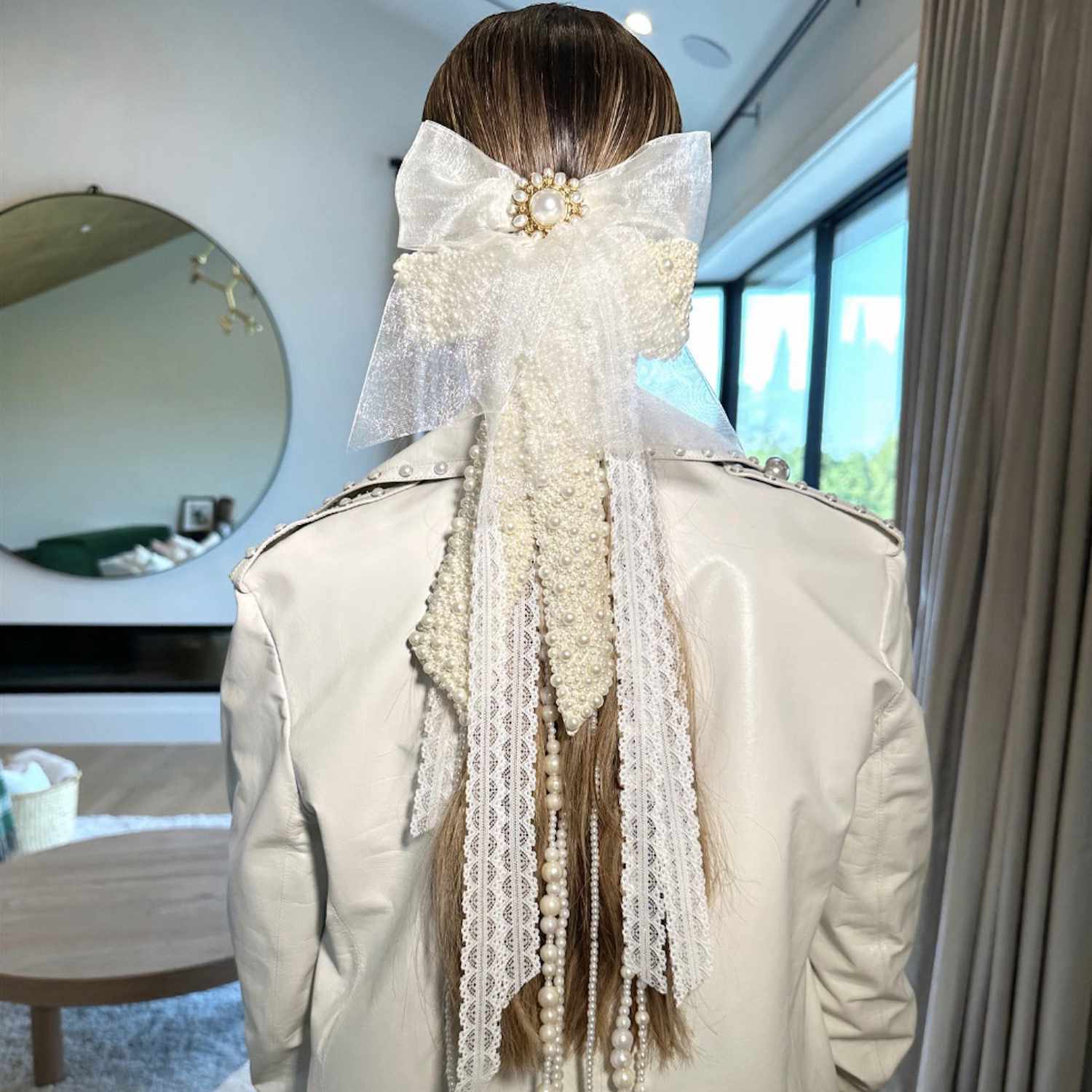 Back view of low ponytail hairstyle accented with bows, white ribbons, and pearl strings