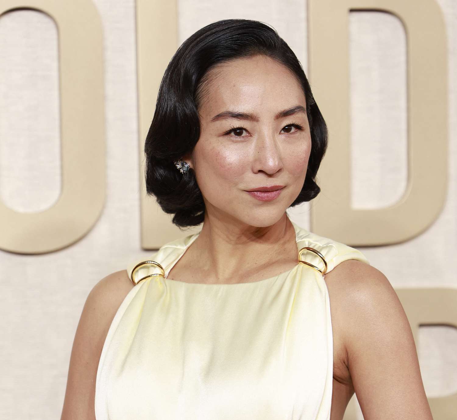 Greta Lee wears a voluminous vintage bob hairstyle and ivory gown with gold detailing