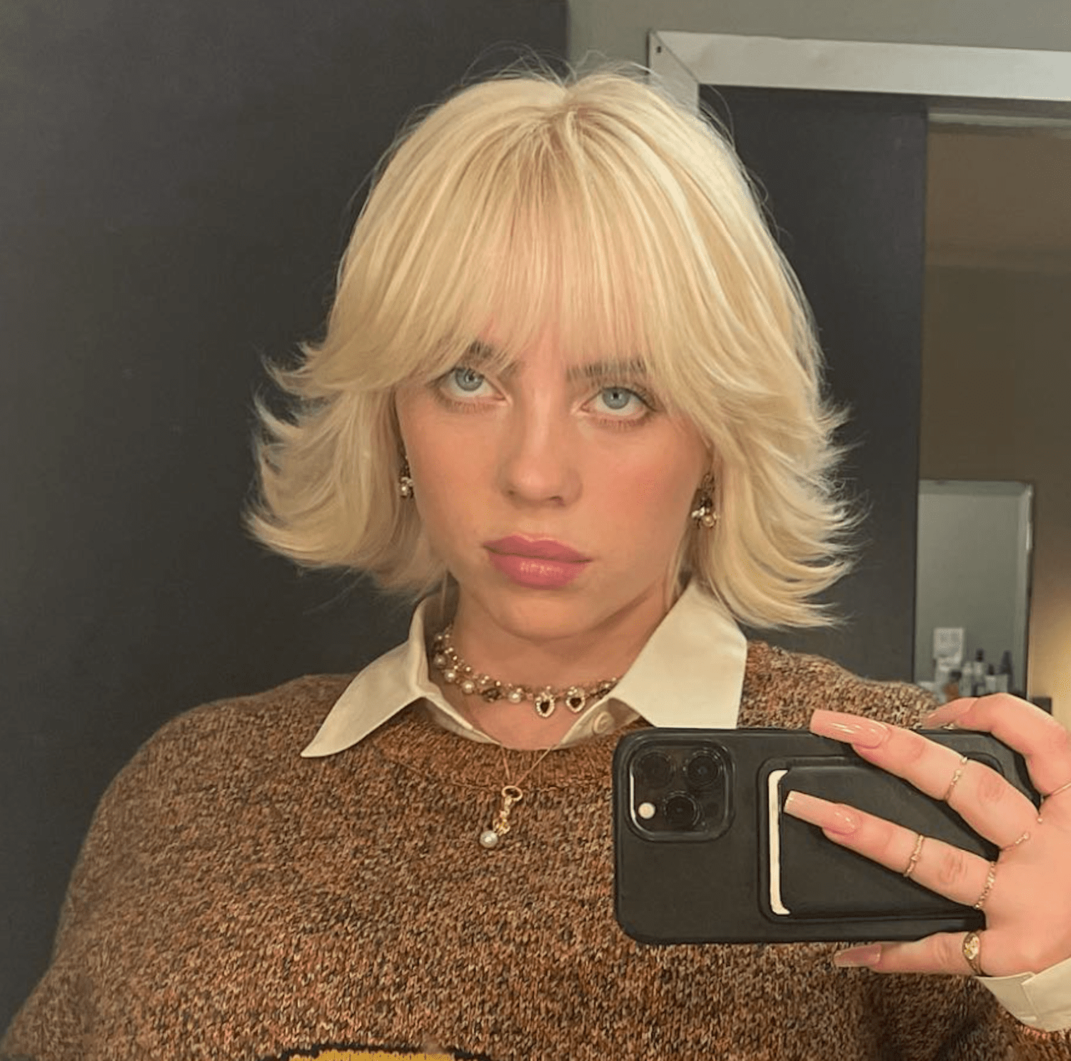 Billie Eilish with flipped-out shaggy bob hairstyle with bangs in mirror selfie