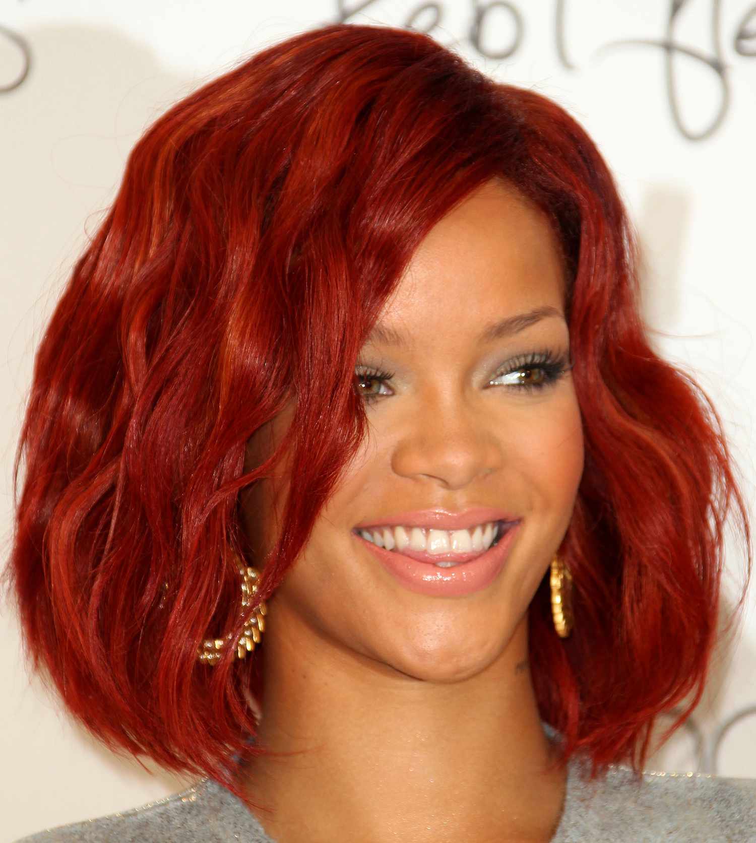 Rihanna wears a red wavy voluminous bob hairstyle and fresh makeup