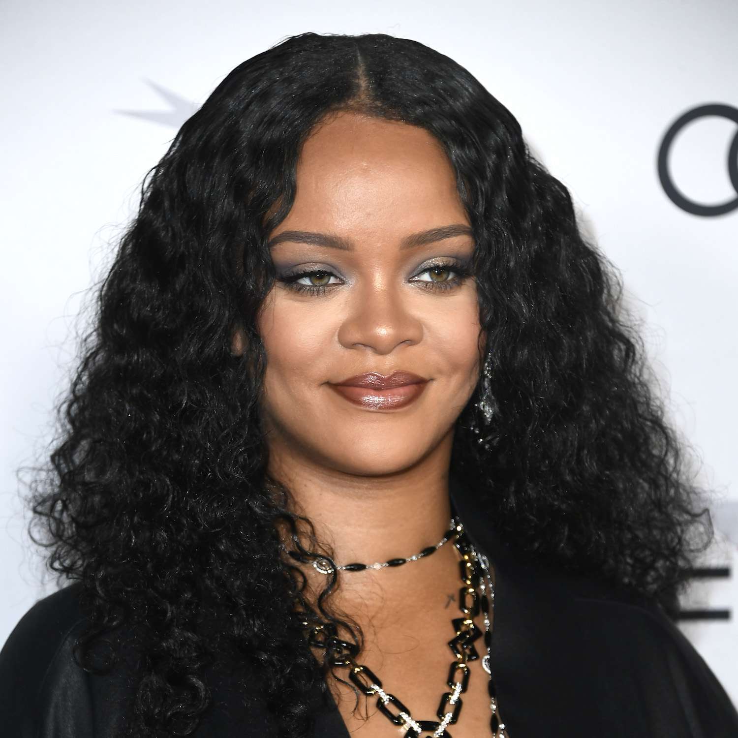 Rihanna wears a long, tousled curly hairstyle with subtle face-framing layers