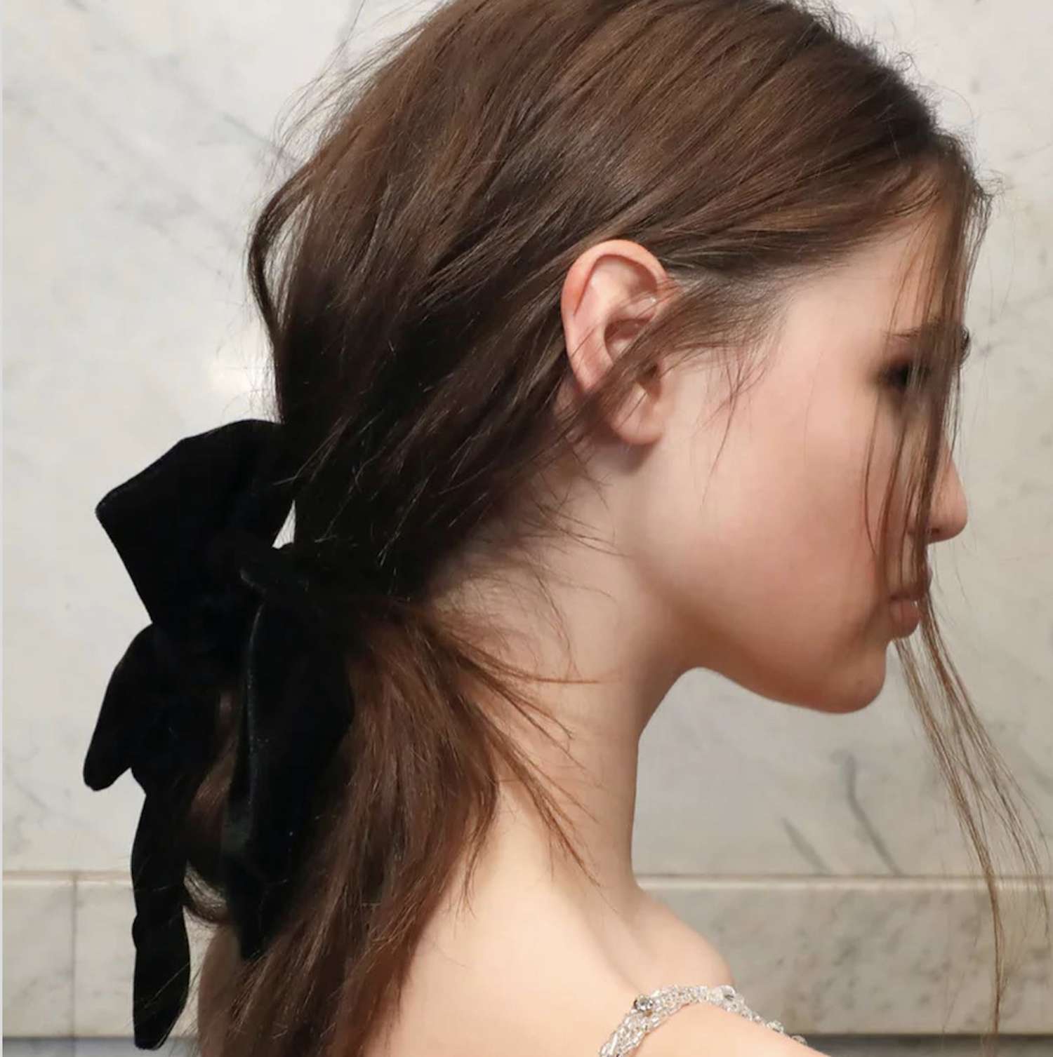 Side view of woman with low tousled ponytail hairstyle with black bow at base