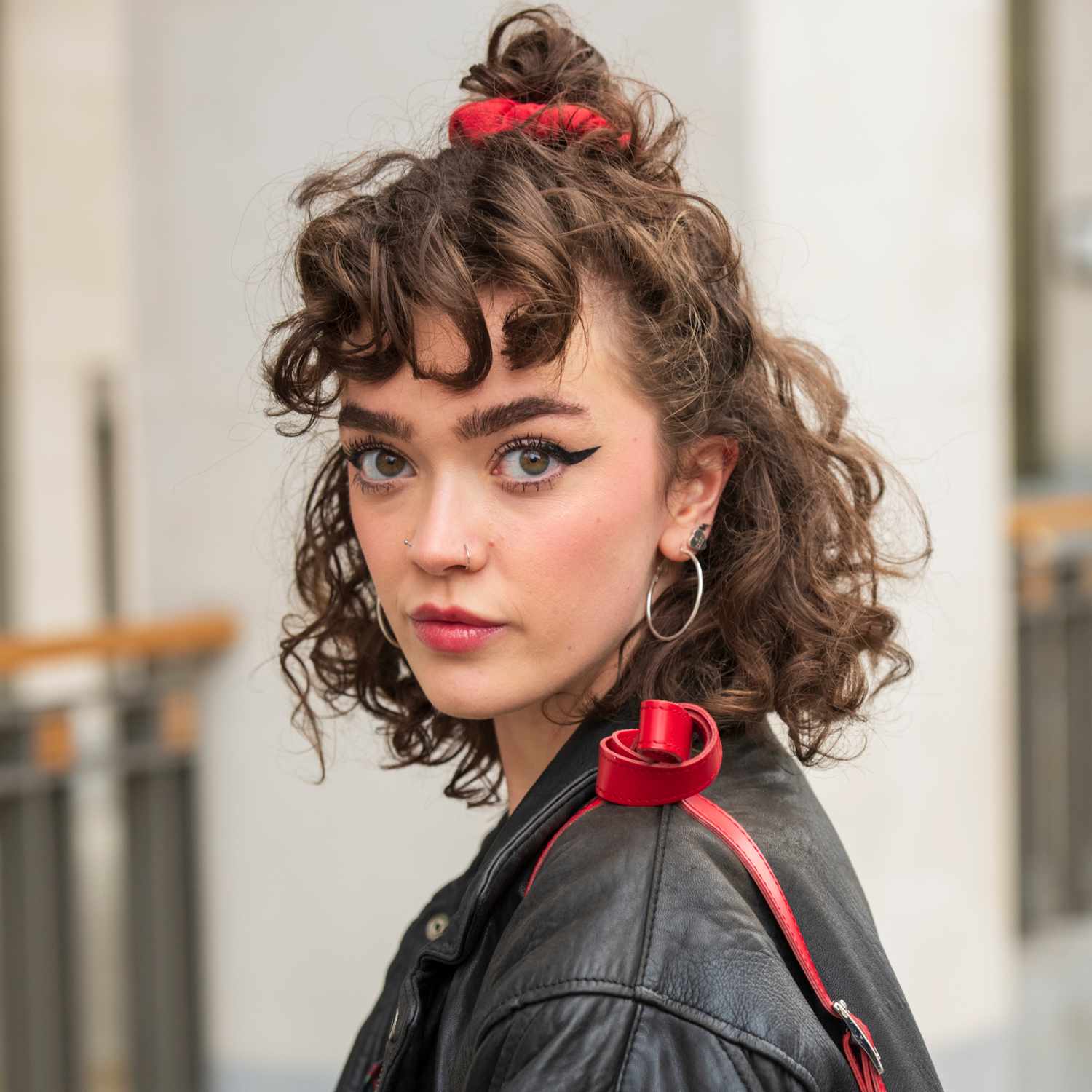 Sophie Seddon looking at camera, zoomed in on face, short bob, bouncy curls, curly bangs, half-up half-down bun secured with red scrunchie