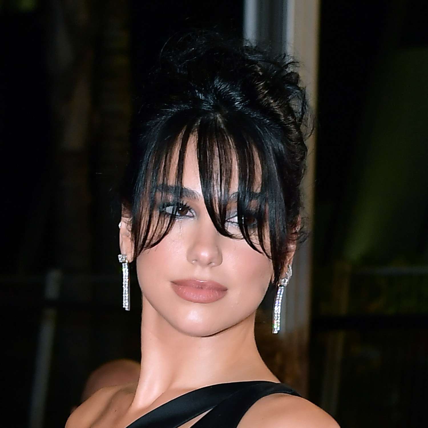 Dua Lipa wears an updo hairstyle with statement curved bangs over her face